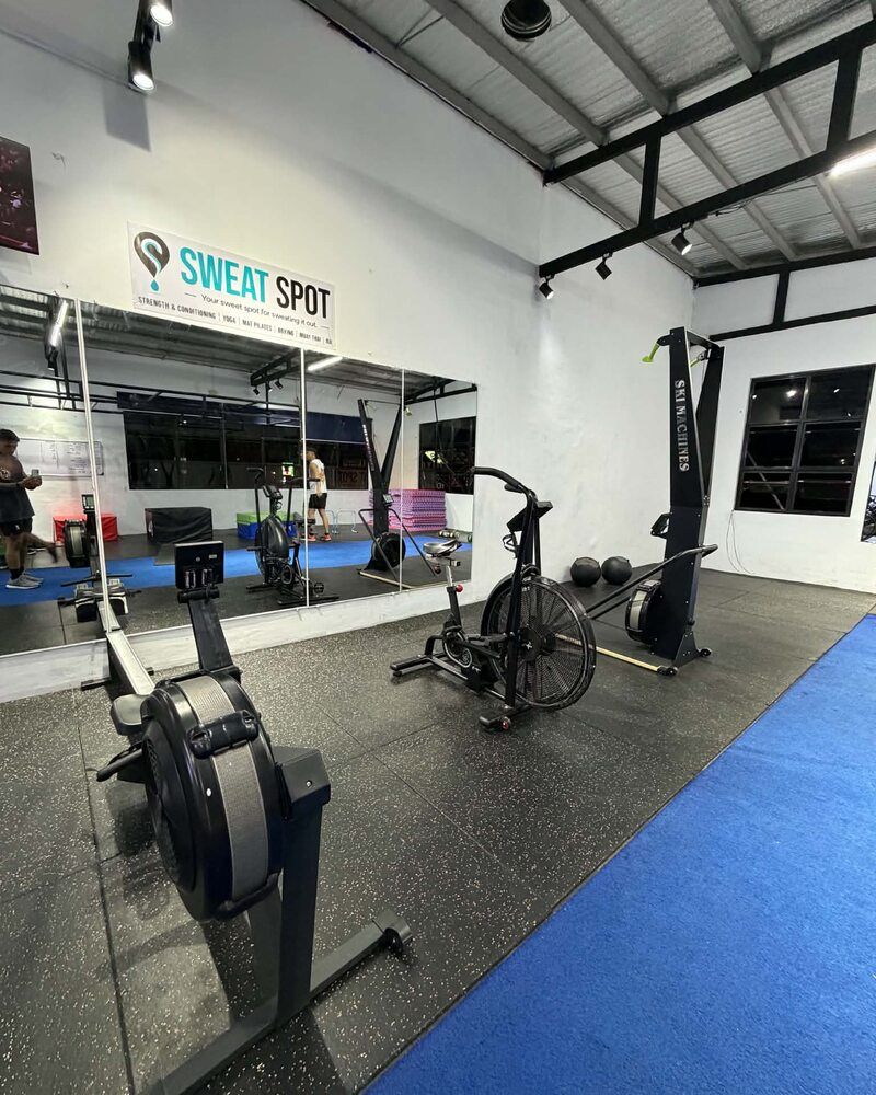 Conditioning area with a rower, an air bike and a ski erg beneath the Sweat Spot wall sign