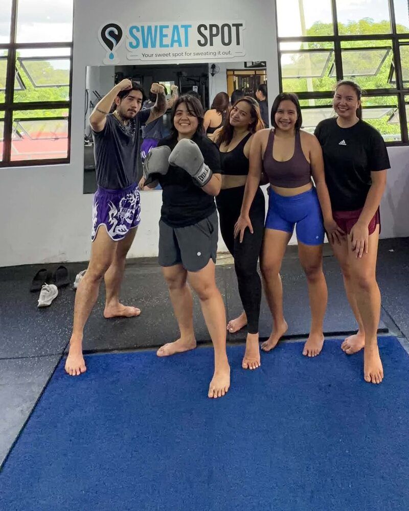 Five members posing together in the Sweat Spot gym, one wearing boxing gloves